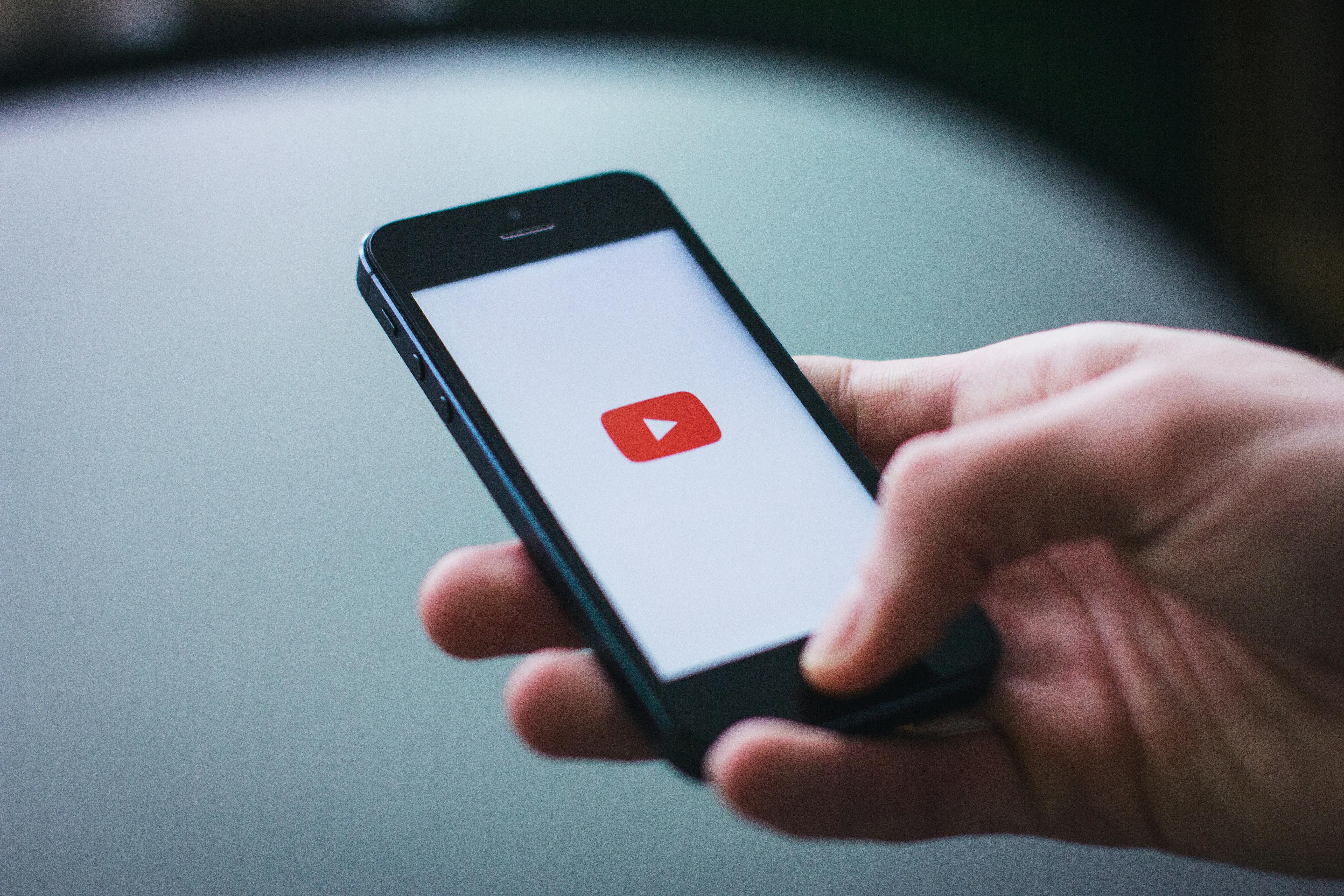 Dłoń trzymająca telefon z wyświetlonym logo YouTube.